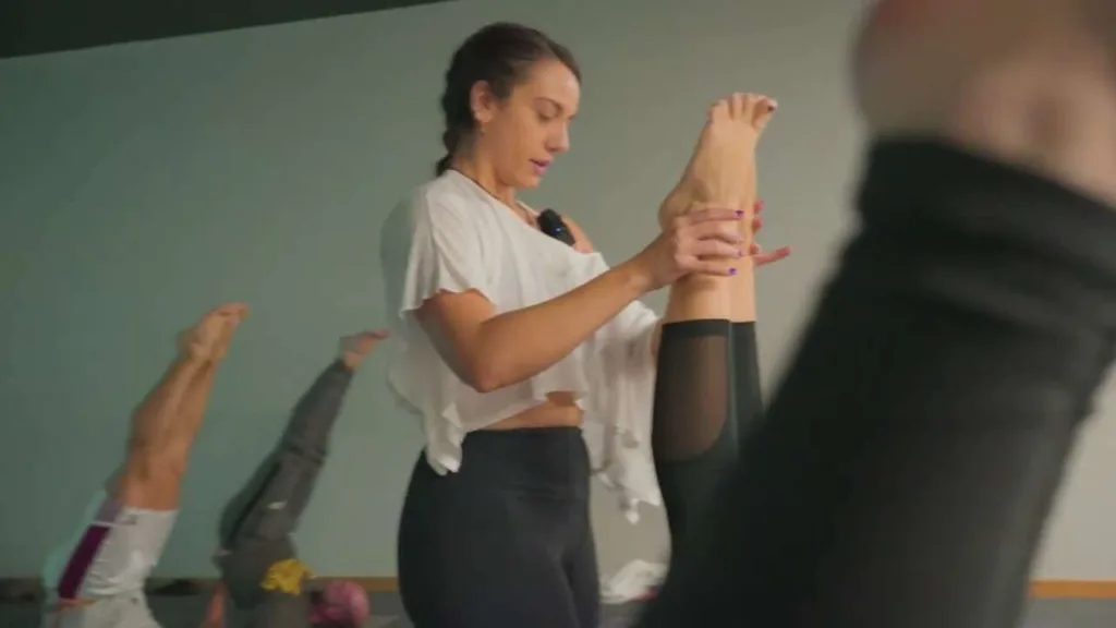 Profesora de la clase de yoga de Colen ayudando a una alumna a ganar rango en una postura de movilidad
